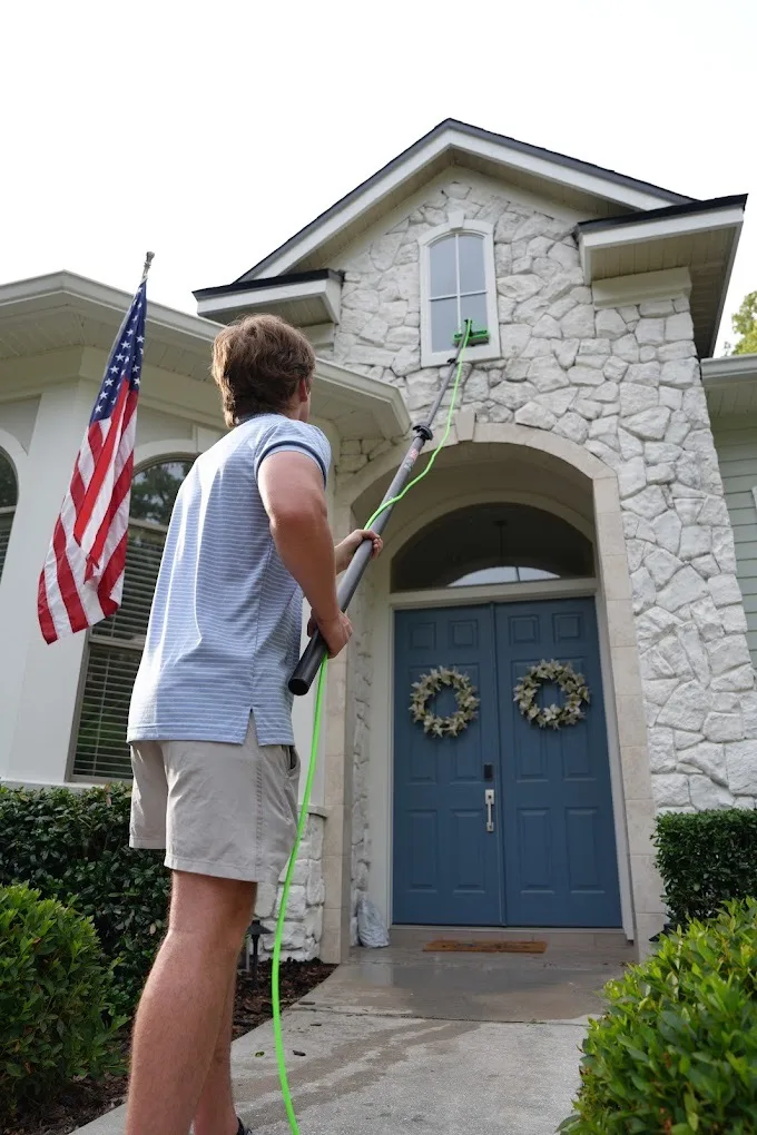 Technician using a water-fed pole to clean second-story windows on a stone Gainesville home