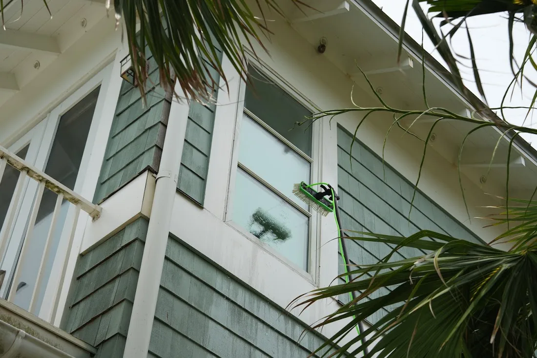 Water-fed pole brush cleaning salt film off an upper-story beach house window